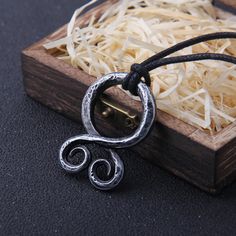 a necklace with an open ring on it sitting in a wooden box next to some straw