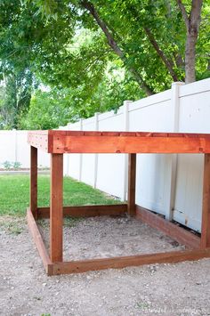 a wooden bench sitting under a tree in the dirt next to a white picket fence