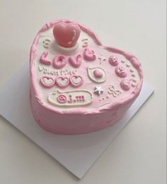 a pink heart shaped cake sitting on top of a piece of paper with writing and decorations