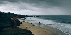 an ocean beach with waves coming in to the shore and dark clouds over the water