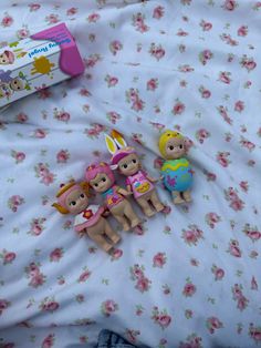 three little dolls sitting on top of a bed next to a tube of toothpaste