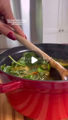 a woman stirring a pot of soup with a wooden spoon