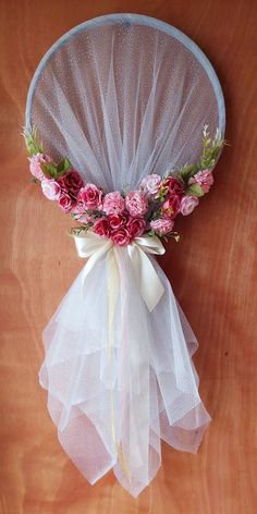 a white net with pink flowers and greenery tied to the side on a wooden table