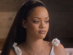 a close up of a person sitting on a couch wearing a white dress and necklace