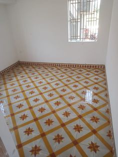 an empty room with yellow and white tiles on the floor, window in the corner