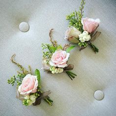 three boutonnieres with pink roses and greenery on a white cloth background