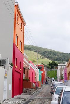 cars parked on the street in front of buildings with colorful doors and windows, along with a hill behind them