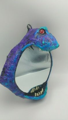 a purple and blue dragon head with red eyes on it's face, sitting in front of a mirror