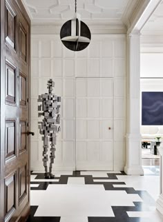 a black and white checkered floor with an abstract sculpture in the center next to a wooden door