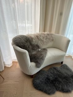 two sheepskin rugs on the floor in front of a chair and window with curtains