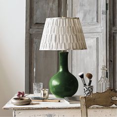 a green vase sitting on top of a table next to a lamp and other items