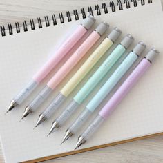 several pens are lined up in a row on a notepad next to an open notebook