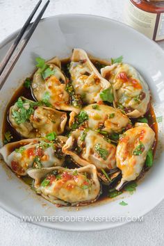 a white bowl filled with dumplings covered in sauce and garnished with green onions