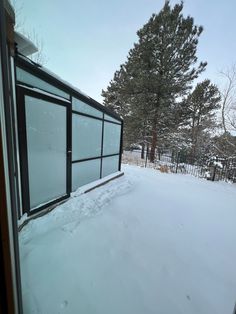 an open window on the side of a house in the snow with trees behind it