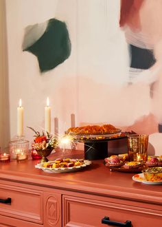 a table topped with lots of food on top of a wooden dresser next to candles