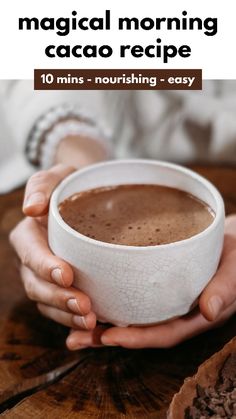 a woman holding a cup of hot chocolate on top of a wooden table with text overlay that reads, the magic morning caco recipe 10 mins - nourishing - easy