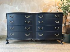 a blue dresser with gold handles and knobs on the drawers is next to a potted plant