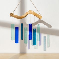 a wind chime hanging from a wooden branch with blue and green glass tubes attached to it