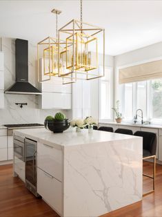 a kitchen with marble counter tops and gold accents on the pendant lights over the island