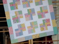 a woman holding up a quilt made with blocks and squares in pastel colors on a wooden fence