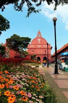 an old church is surrounded by flowers and greenery on the side of the road