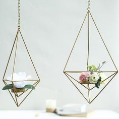 two hanging planters with flowers in them on a white table next to a candle