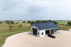 a car is parked in front of a white house with a black roof and two brown garage doors