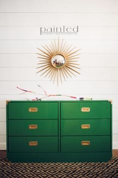 a green dresser sitting in front of a wall with a sun mirror on top of it