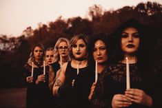 a group of women holding candles in front of their faces while wearing black clothing and makeup