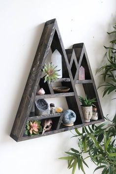 a triangle shaped shelf with plants and rocks on the bottom, in front of a white wall