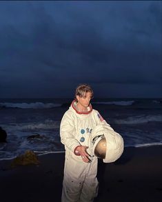 a man in an astronaut suit standing on the beach at night with his helmet up