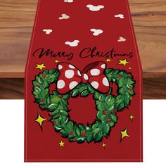 a red christmas table runner with a mickey mouse wreath and stars on the front, along with merry christmas written in black ink