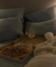 a pizza sitting on top of a bed next to a glass of wine