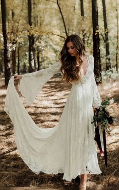 a woman in a white dress is walking through the woods with her long sleeves open