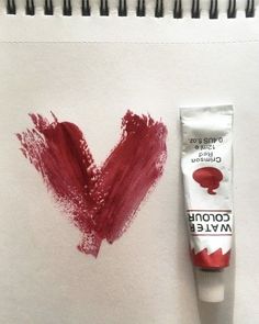 a drawing of a red heart on paper next to a tube of toothpaste