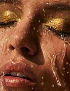 a woman's face covered in water with gold eyeshadow and glitter on it