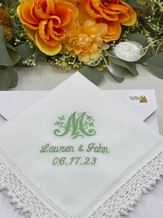 a white napkin with a monogrammed initial on it next to some orange flowers