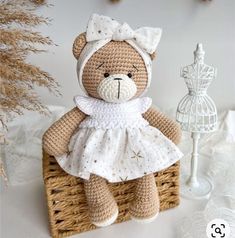 a crocheted teddy bear in a white dress sitting on a wicker basket