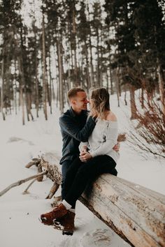 a man and woman sitting on a log in the snow with their arms around each other