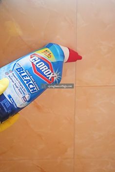 a hand holding a bottle of cleaner on top of a tile floor with a sponge