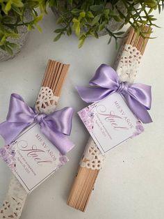 two wedding favors tied with purple ribbon and matching matchesticks are sitting next to a potted plant