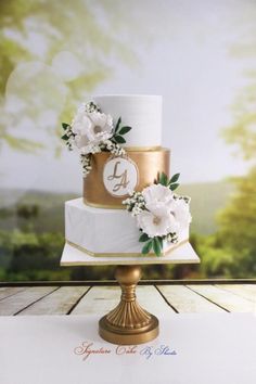 a three tiered wedding cake with white flowers on the top and gold trimmings