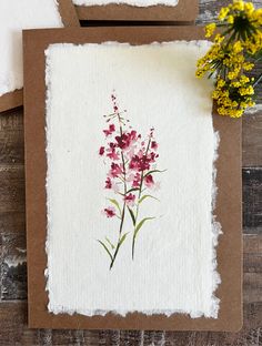 two cards with watercolor flowers on them sitting next to each other in front of a wooden background