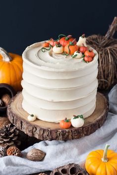 a white cake sitting on top of a wooden table next to pumpkins and pine cones