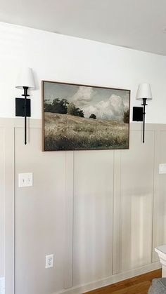 a painting hanging on the wall above a couch in a room with white walls and wood flooring