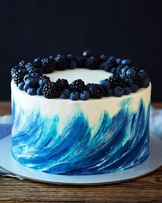 a blue and white cake with blackberries on top is sitting on a wooden table