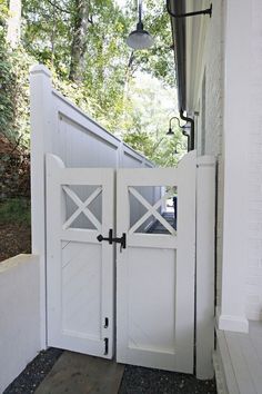 an open white door leading to a house with a light on the side and trees in the background