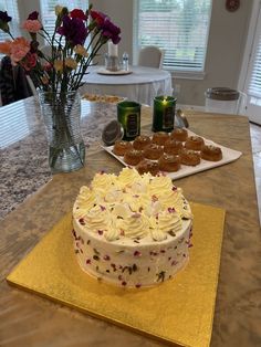 a white cake sitting on top of a table next to some flowers and cans of beer