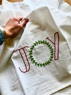 someone is stitching the word joy on a white towel with red thread and green leaves