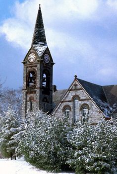 an old church with a clock tower in the middle of it's snowing grounds